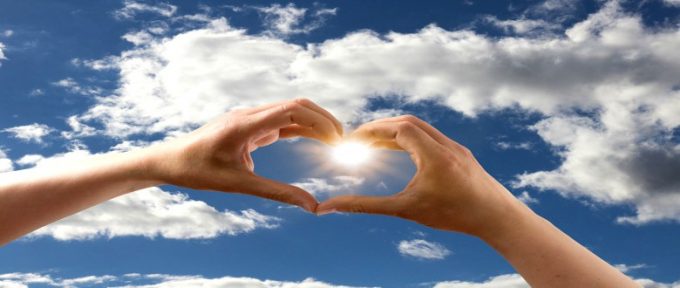 heart symbol with hands up to the sun in the cloudy sky