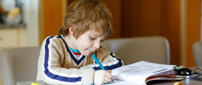 young boy using his colouring in book with his blue pen