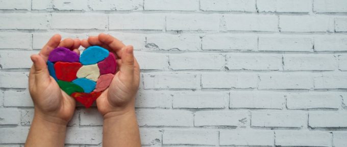 childs hands holding a multicoloured heart