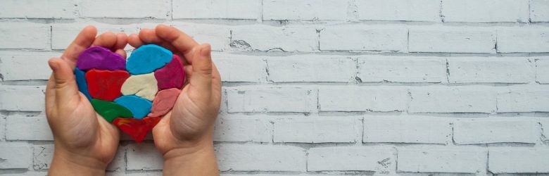 childs hands holding a multicoloured heart