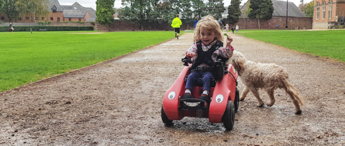 young girl riding a wizzybug with dog in the background