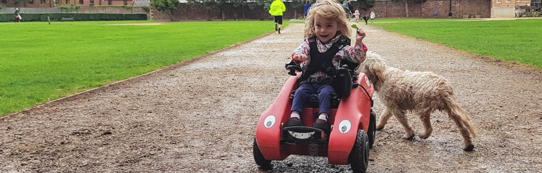 young girl riding a wizzybug with dog in the background