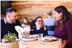 young person in robotic dining companion with people either side smiling