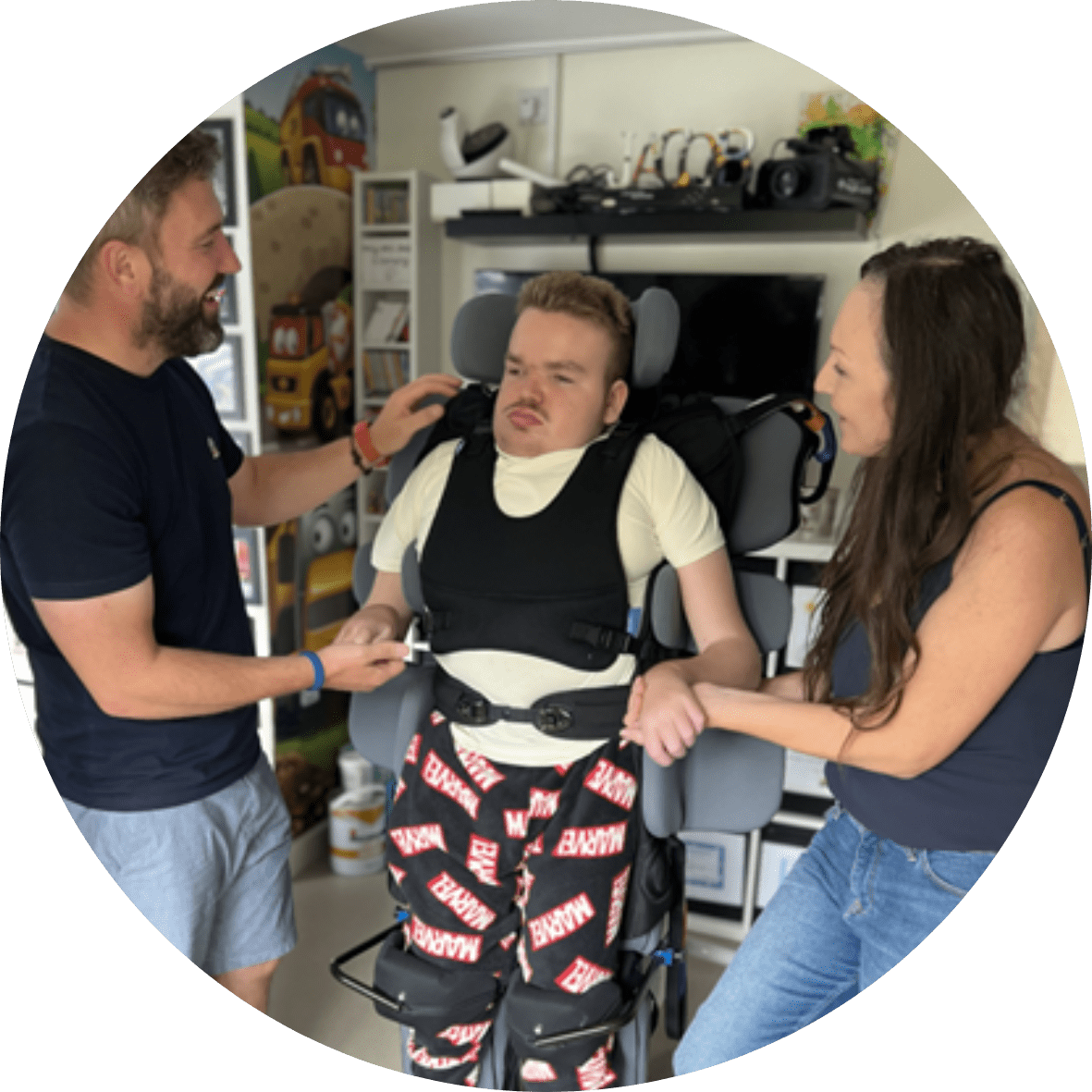 A photograph of Jacob in his standing frame with his parents either side of him.